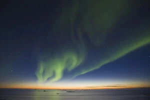 The Big Dipper hangs over curtains of green Aurora Borealis dancing over the iceberg