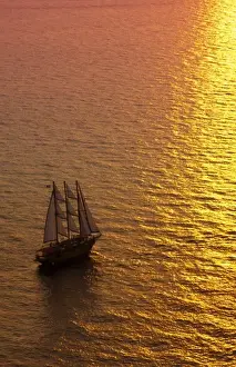 Prints of Big masked sailboat sailing in sunset of beautiful Oia in Santorini Greece in Greek Islands from above on cliff into water Images Dated 2028 September: Big masked sailboat sailing in sunset of beautiful Oia in Santorini Greece in Greek