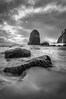 Black and white vertical of swirling water around rocks on a beach