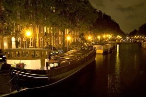 Boats docked at night along a canal near the Amstel River in Amsterdam, Netherlands