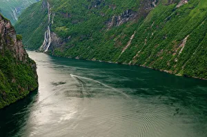 Seven Sisters Prints: A boat's wake ripples Geirangerfjord as it winds through forest covered sheer cliffs and mountains