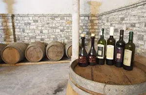 Mature Prints: Bottles on top of a barrel, with barriques in the background: Raki me Arra grappa type of spirit