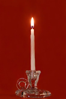 Burning Prints: Burning candle in a glass candle holder on red background