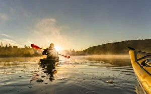British Columbia Collection: Canada, British Columbia. A kayaker paddles in sunlit early morning mist on a Canadian