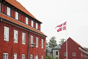 Inti St Clair Prints: Copenhagen, Denmark - A Danish flag is flying in front of red military barracks