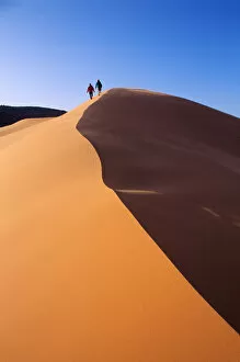 A couple walks along the crest of a golden sand dune in Coral Pink Sand Dunes State Park