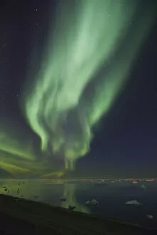 Curtains of Aurora Borealis are reflected in a perfectly calm Arctic Ocean, dotted