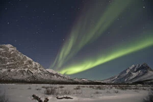 Curtains of green aurora borealis fill the sky over high peaks of the Central Brooks
