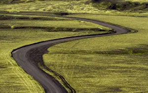 Images Dated 24th July 2012: Europe, Iceland. Black dirt road curves through green countryside