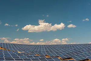 Sustainable Energy Prints: A field of solar panels at a solar power plant under a blue sky with puffy white clouds