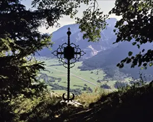 Belief Prints: Germany, Bavaria. A wrought-iron cross looks down on a peaceful valley in Bavaria, Germany