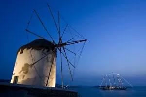 Greece, Mykonos, Hora. Floodlit windmill in foreground and illuminated luxury yacht