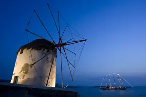 Hora Prints: Greece, Mykonos, Hora. Floodlit windmill in foreground and illuminated luxury yacht