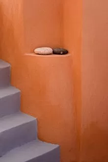 Greece, Santorini, Thira, Oia. Grey stairs contrast with orange wall and two rocks on ledge