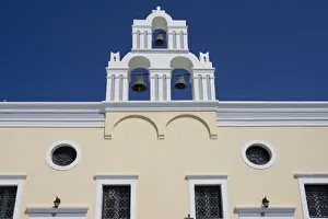 Greece, Santorini. Yellow church wall and white bell tower against dark blue sky