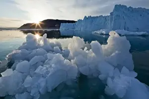 Images Dated 12th June 2010: Greenland, Ilulissat, Setting midnight sun lights icebergs and blue ice face of Eqip