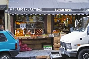 A grocery store with froits and vegetables displayed on the pavement. Cars parked in front