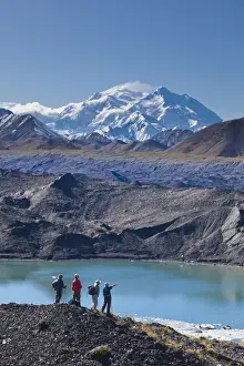 Gravel Prints: A group of hikers stand on moraine next to a glacial meltpond at the edge of the Muldrow Glacier
