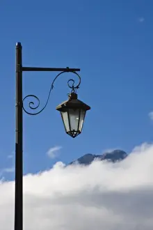 Guatemala, Antigua. Lamp post with Volcano Agua in background covered with clouds