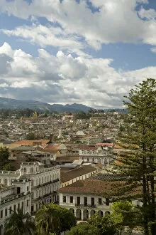Historic buildings with red tile roofs, palm trees, and mountains in distance, Cuenca