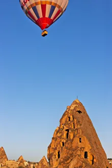Hot air balloon over houses carved into rock formations, Uchisar, Cappadocia, Turkey