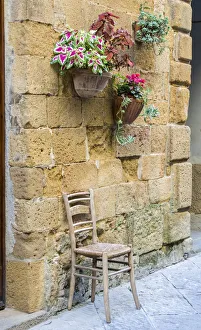 Images Dated 16th April 2021: Italy, Tuscany. Chair and flower pots outside the entrance to a shop in a village in