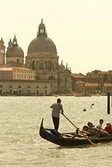 Riverfront Prints: Italy; Venice. A gondolier ferries tourists on the Grand Canal in Venice with the massive church