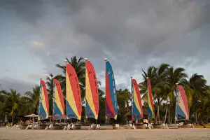 Jamaica, Negril, Setting sun lights row of sailboats at tourist resort along white