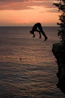 Images Dated 23rd April 2007: Jamaica, Negril, Silhouette of young man leaping from from cliff above Pirates Cave