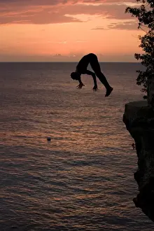 Adventurous Prints: Jamaica, Negril, Silhouette of young man leaping from from cliff above Pirates Cave