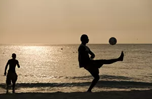 Jamaica, Negril, Silhouette of young men playing soccer along Caribbean Sea