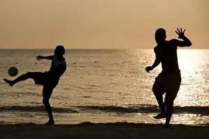 Jamaica, Negril, Silhouette of young men playing soccer along Caribbean Sea