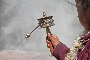 Tibetan Prints: Little Tibetan girl praying with prayer wheel and smoke from incense in Drepung Monastery