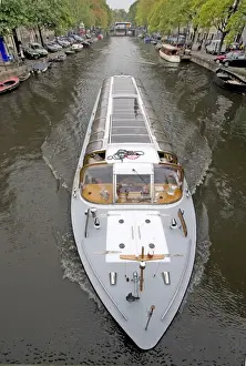 Marilyn Parver Prints: A long glass topped tour boattravels down a boat lined canal