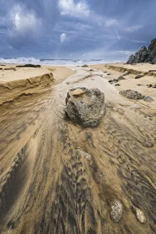 Wide Angle Prints: Low angle of a stream flowing around a rock heading into the ocean with stormy skies