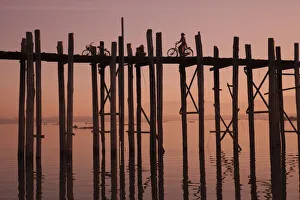 Bicycle Prints: Monk walking at sunrise over the lake near wooden footbridge