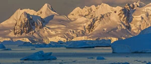 Morning light shines on the mountains of Antarctica, while the icebergs in the ocean