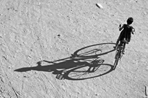 Myamar, Bagan, Young boy riding a huge bike and his long shadow on a sandy field