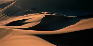 Flowing Prints: Namibia, Namib Desert, Setting sun lights curving sand dunes near coastal city of