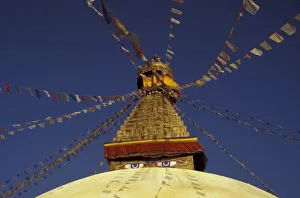 Nepal, Kathmandu. Under prayer flags, watchful eyes of Buddha gaze from Bodhnath Stupa, c