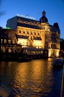 NH Doelen Hotel with lights on at night along the Amstel River in Amsterdam, Netherlands