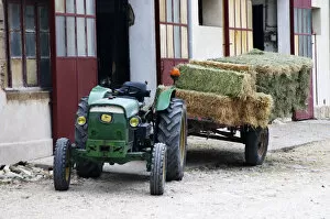 An old rusty green tractor John Deere drawing a cart filled with hay bales parked
