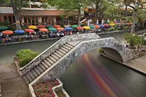 Outdoor cafe along River Walk and boat in motion passing under bridge over San Antonio River