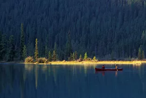 Images Dated 19th September 2006: Two people paddle in a canoe in the early morning light, with lush forest behind them