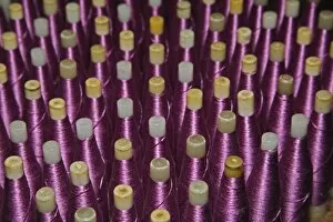 Purple silk thread wound on bobbins stacked in rows at a silk weaving factory, Chiang Mai