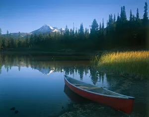 Red canoe pulled on shore of Sparks Lake with early morning light filtering across
