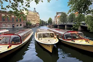 Miva Stock Prints: Refurbished old canal cruise boats moored along Amstel canal in Amsterdam, The Netherlands