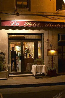 The restaurant Le Petit Bedon at night with the waiter standing inside the door. Avignon