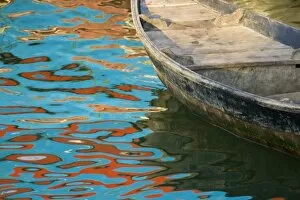Rowboats float in water reflecting distinctive red and blue fishing boats, Nha Trang