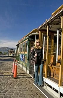 San Francisco pretty blond female in sunglasses holding on to cable car at Friedel